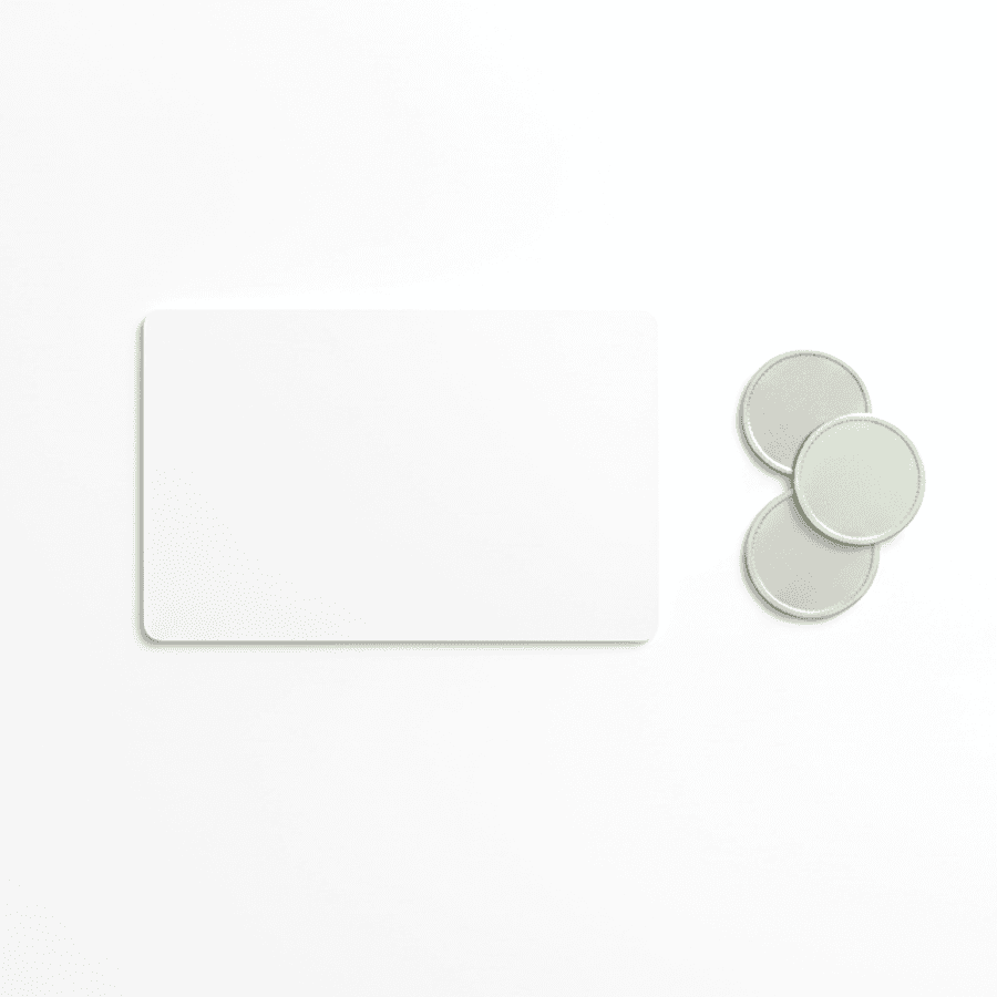 A blank white payment card lying flat beside three small pale green and silver coins on a white surface.